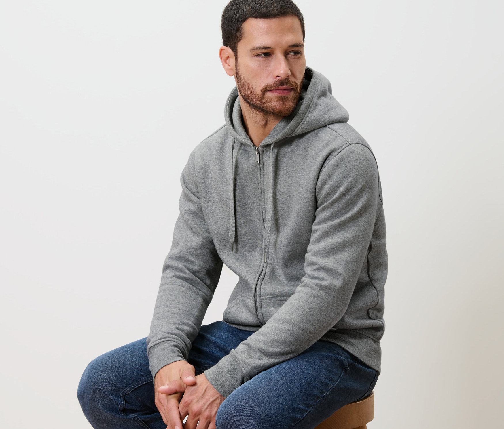 Un homme est assis sur un tabouret et porte une veste à capuche grise.