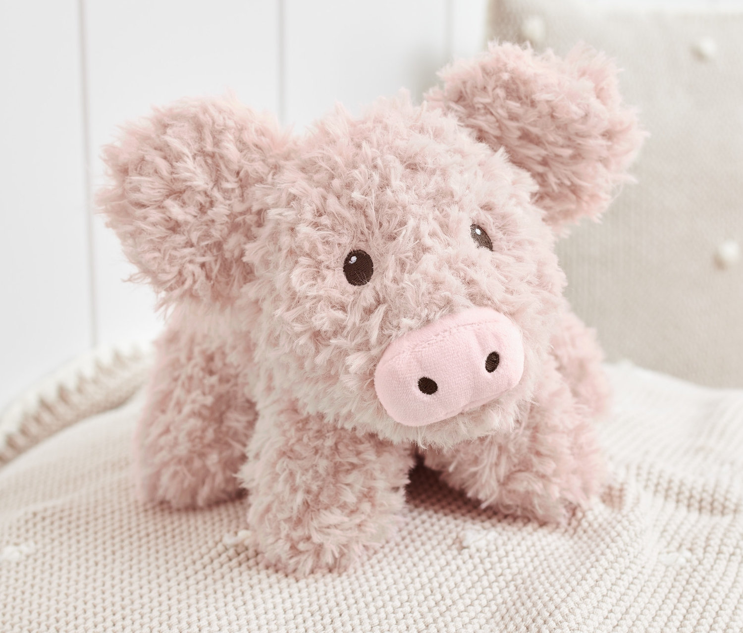 Un animal en peluche « Cochon » est allongé sur une couverture tricotée.