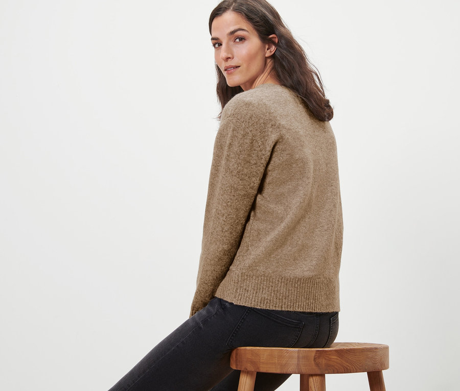 Femme assise sur un tabouret en bois portant une jaquette en maille avec de la laine.