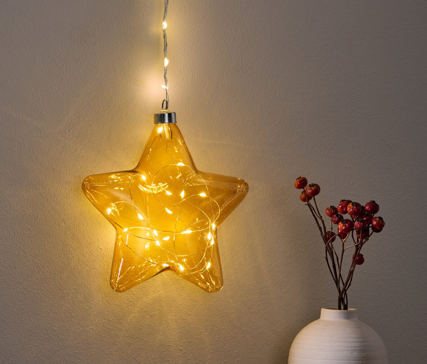 Une étoile à LED suspendue brille au-dessus d'une table à côté d'un vase avec des baies rouges.