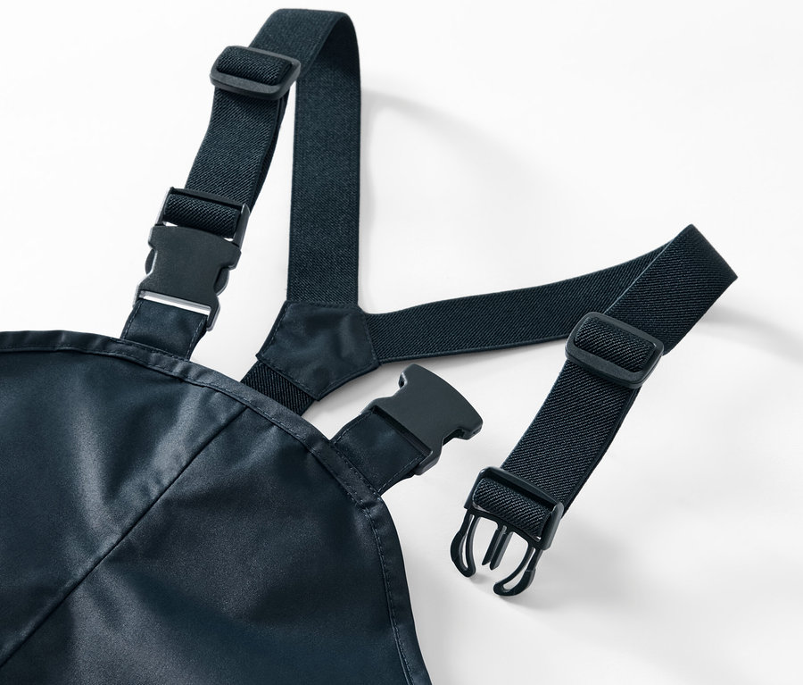 Gros plan sur un pantalon de pluie pour enfant avec des bretelles élastiques noires et des boucles en plastique sur un fond blanc.