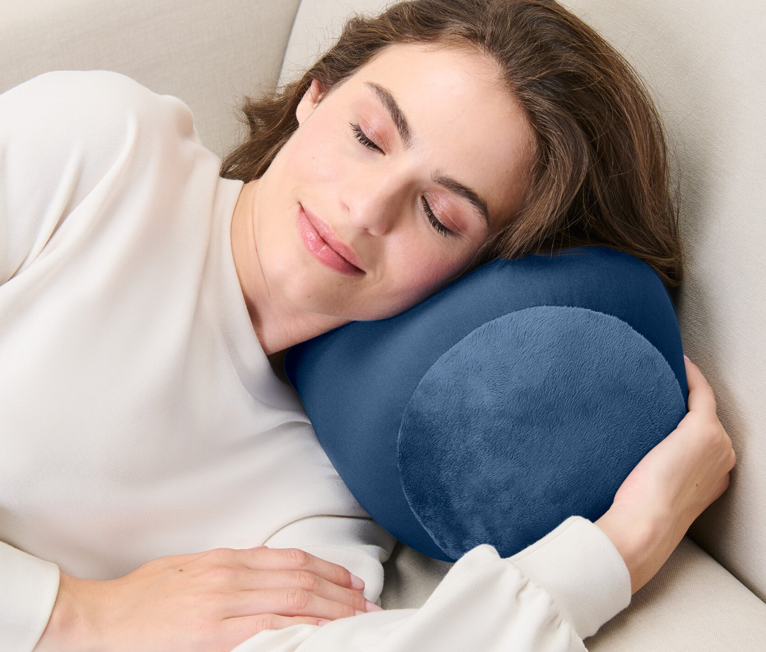 Une femme dort sur un canapé beige avec un coussin de relaxation.