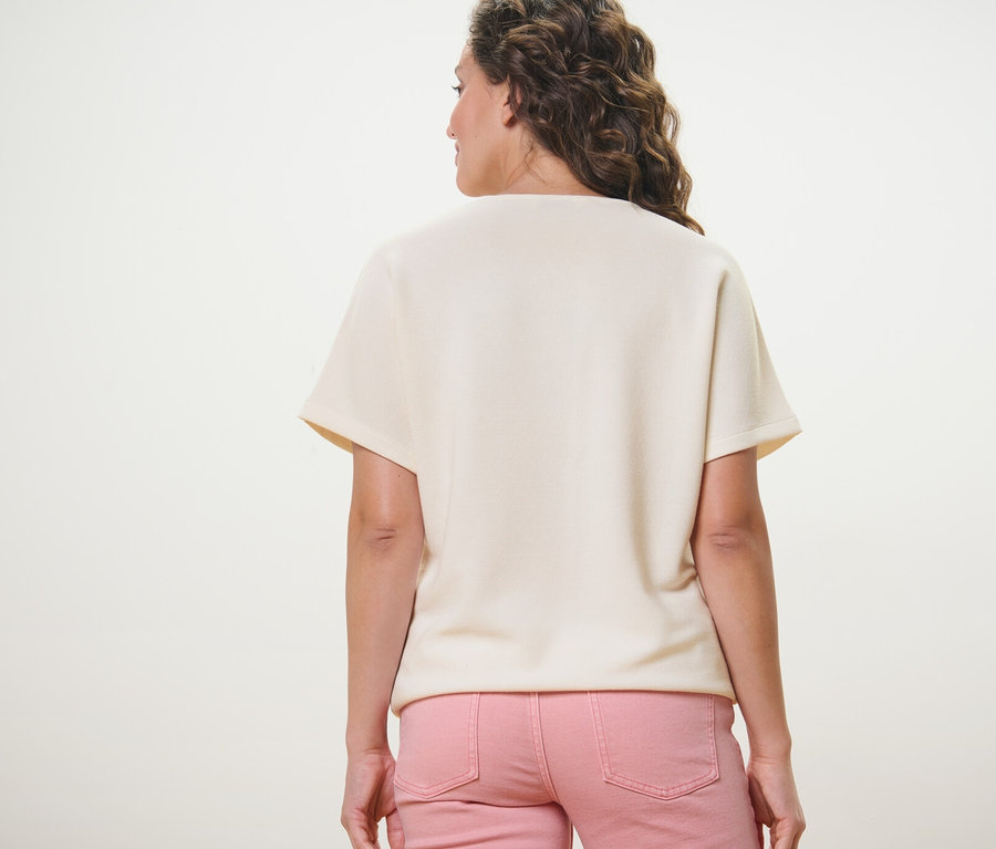Vue arrière d'une femme portant un chemisier blanc crème et un pantalon rose.