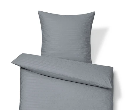 Une parure de lit en seersucker grise de taille standard et grande taille est disposée sur un fond blanc.