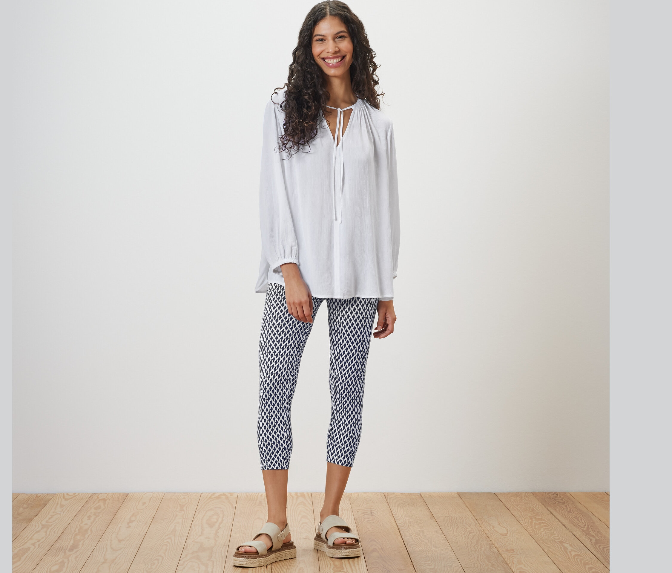 Femme debout portant un chemisier blanc et un legging 3/4 imprimé.