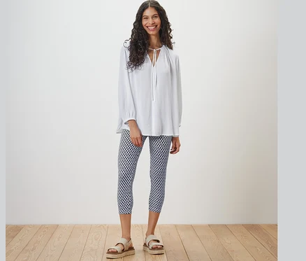 Femme debout portant un chemisier blanc et un legging 3/4 imprimé.