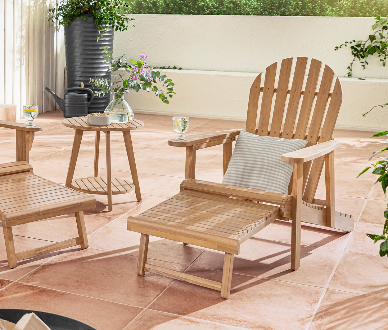 Un fauteuil de relaxation Adirondack double et simple avec repose-pieds extensible sont placés sur une terrasse avec 2 coussins d’extérieur en lin haptique.