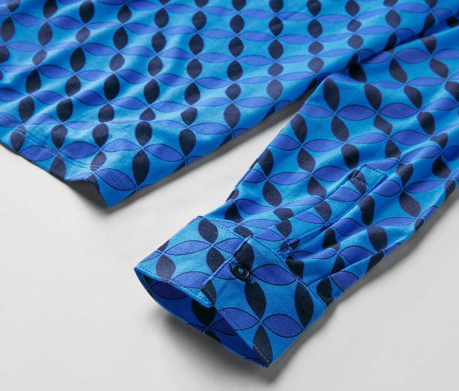 Détail d'une blouse bleue à motifs avec patte de boutonnage au poignet.