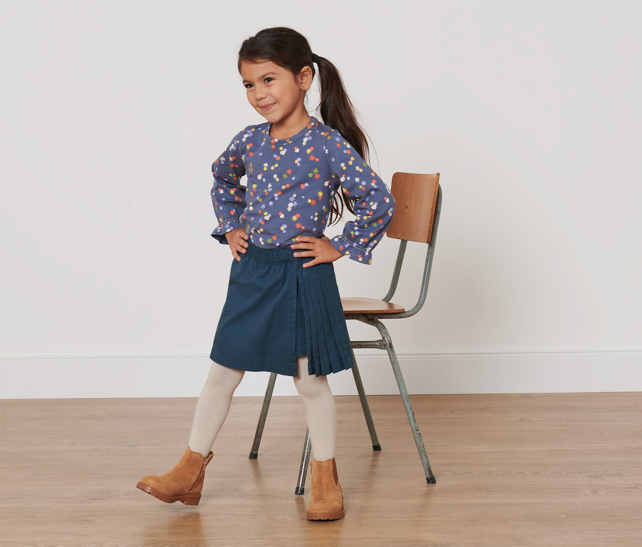 Une fille pose dans un chemisier bleu à fleurs et une jupe kilt bleu marine.