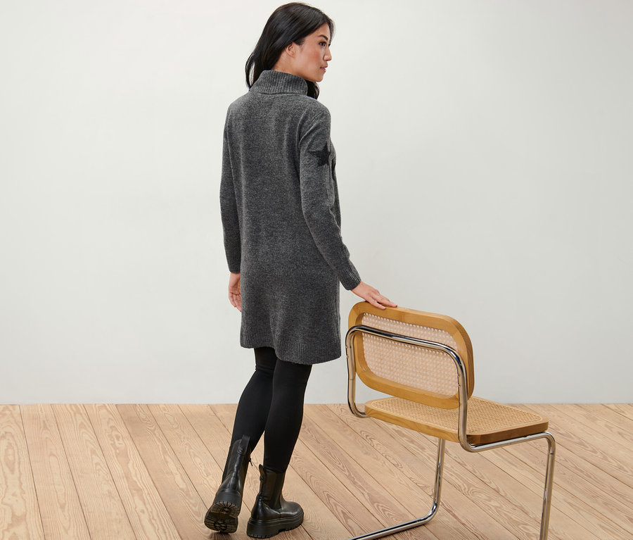 Une femme, vue de dos, pose en robe en maille à col roulé.