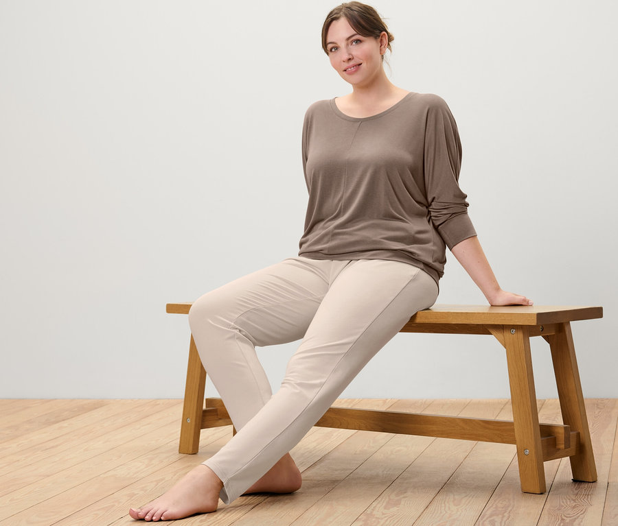 Femme assise sur un banc portant un t-shirt de sport et de yoga taupe et un pantalon en sweat beige.