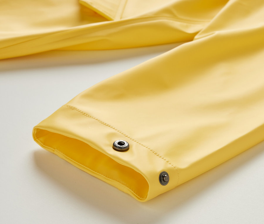 Gros plan sur la manche jaune d'un parka de pluie « ciré » avec des boutons-pression.