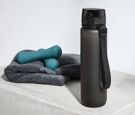 Une gourde noire est posée sur une surface grise à côté d'une serviette et d'haltères.