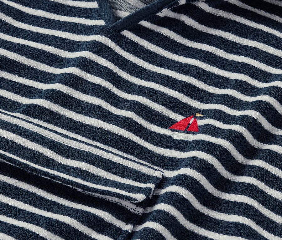 Gros plan sur un poncho en éponge bord de mer rayé bleu et blanc avec une petite broderie rouge de voilier.