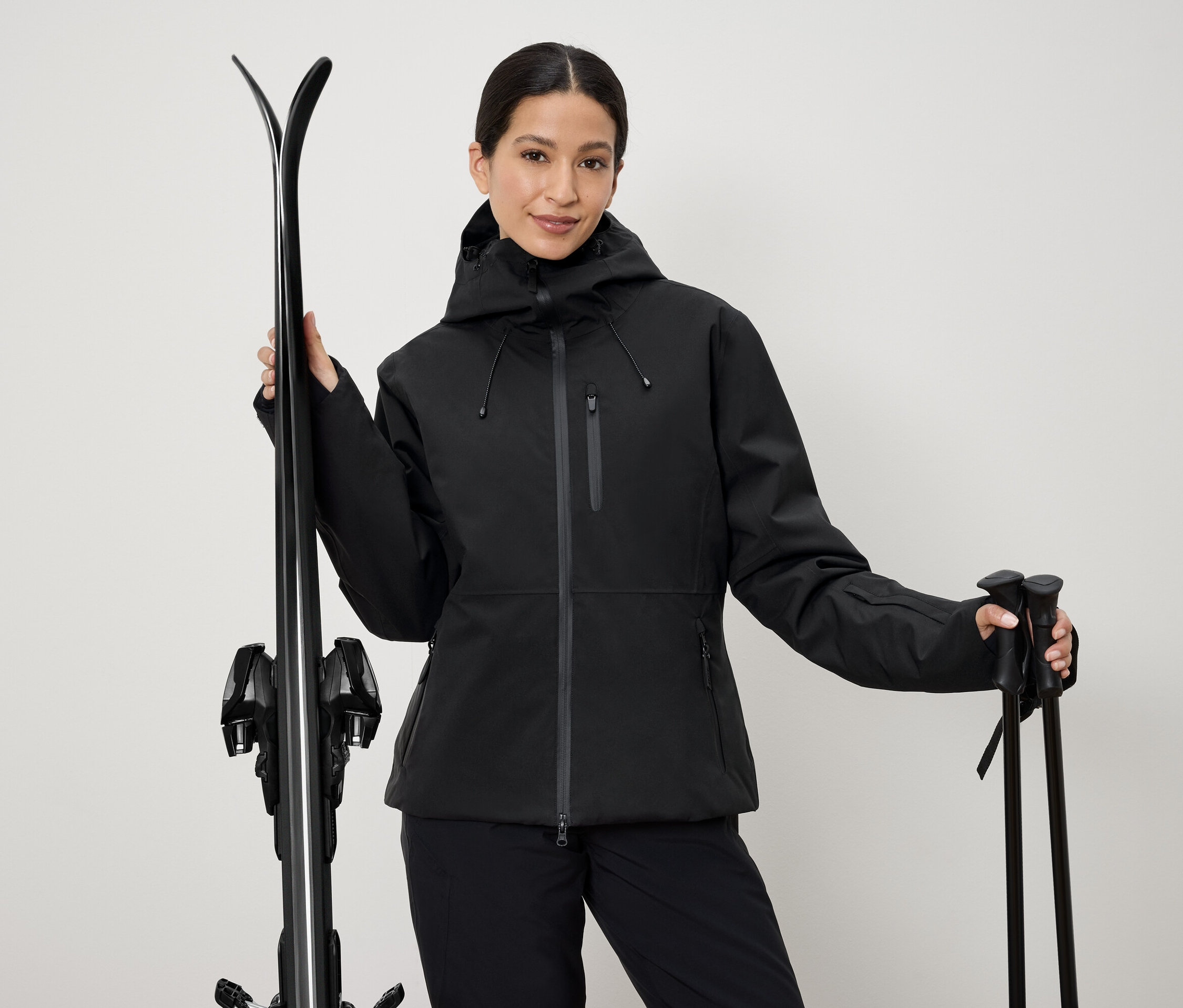 Femme en veste de ski noire tenant des skis et des bâtons.