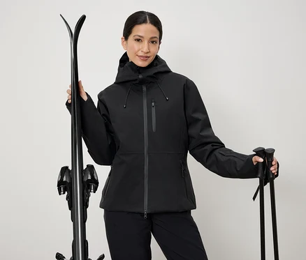 Femme en veste de ski noire tenant des skis et des bâtons.