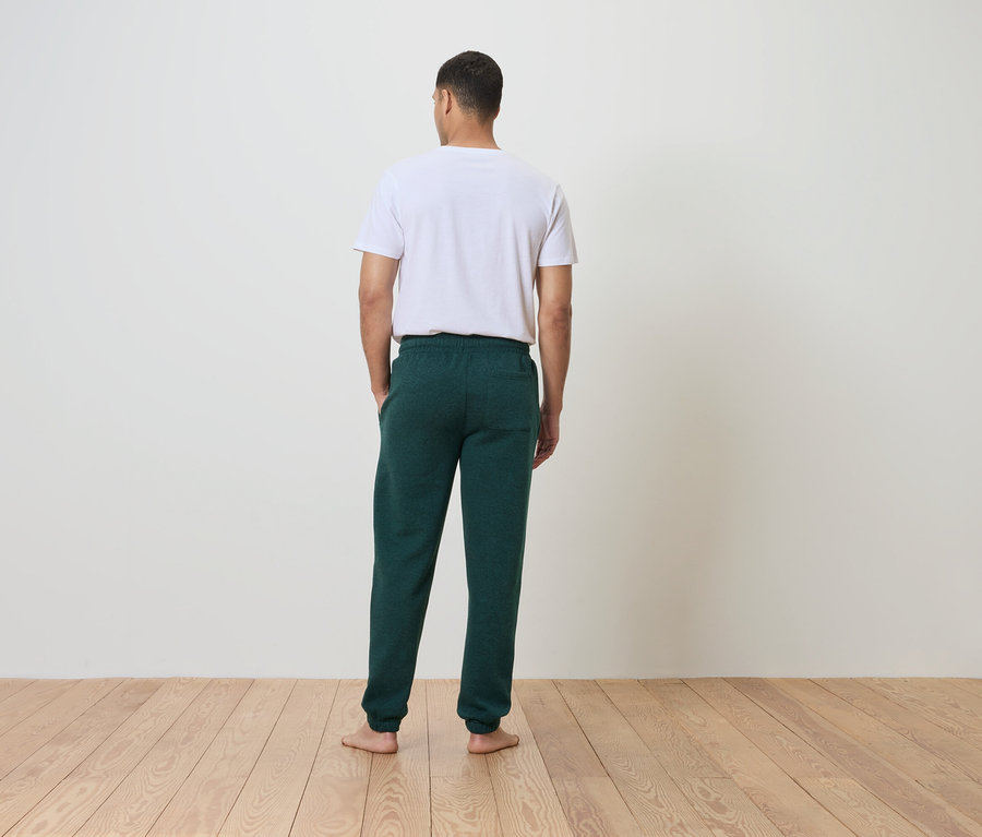 Un homme, dos à la caméra, porte un t-shirt blanc et un pantalon de survêtement vert.