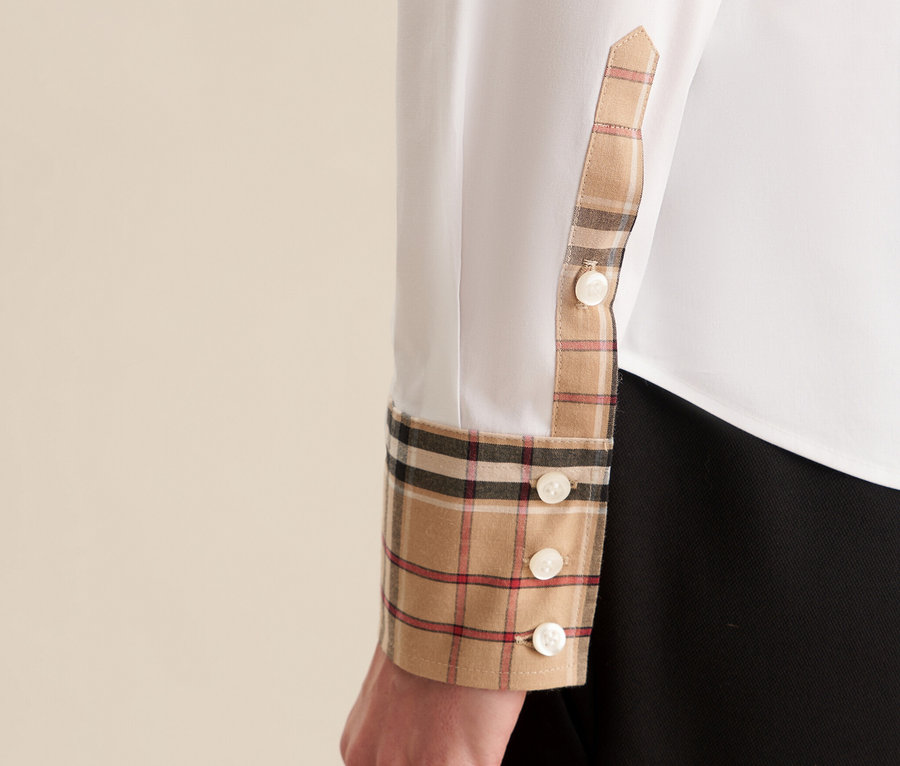 Détail d'une blouse blanche Seidensticker en popeline avec motif à carreaux sur le poignet et les boutons.