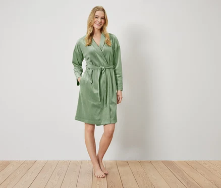 Une femme debout porte un peignoir vert clair avec une ceinture.
