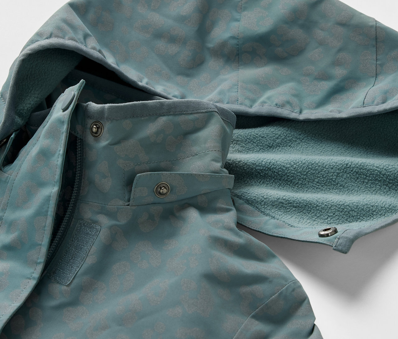 Détail d'une veste de pluie thermique pour enfant avec éléments réfléchissants. La veste a une capuche et une fermeture éclair.