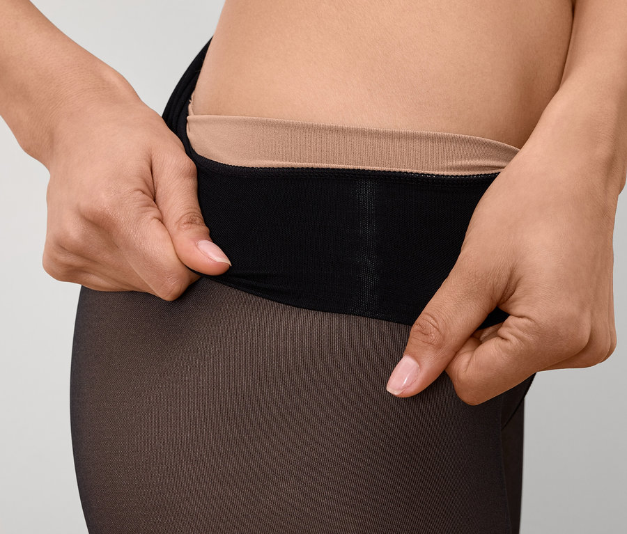 Gros plan d'une femme remontant un collant noir avec une ceinture couleur chair.
