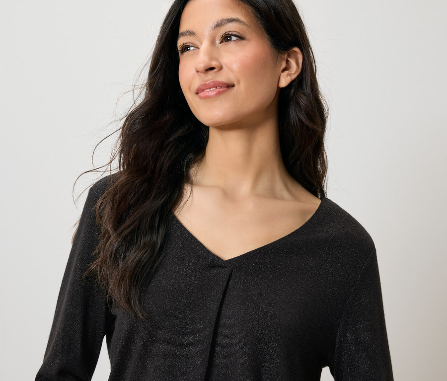 Portrait d'une femme souriante aux longs cheveux noirs, portant un haut noir scintillant à col en V.