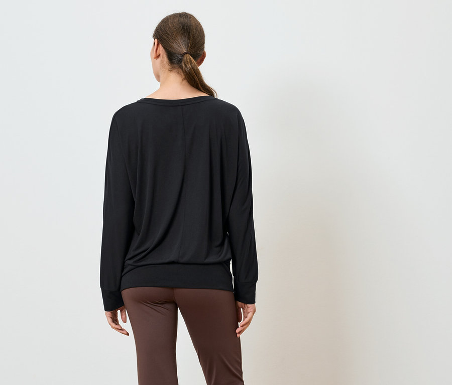 Une femme, vue de dos, porte un t-shirt noir à manches longues et un pantalon marron.