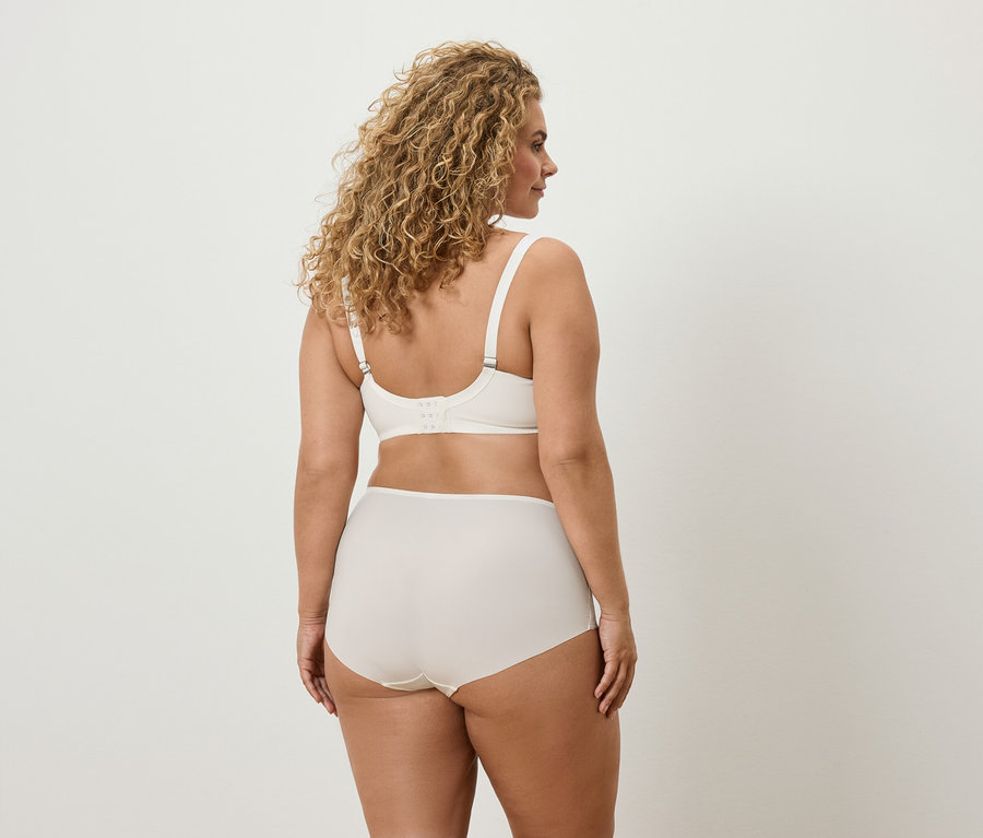 Vue arrière d'une femme aux cheveux bouclés portant un soutien-gorge et une culotte couleur crème.