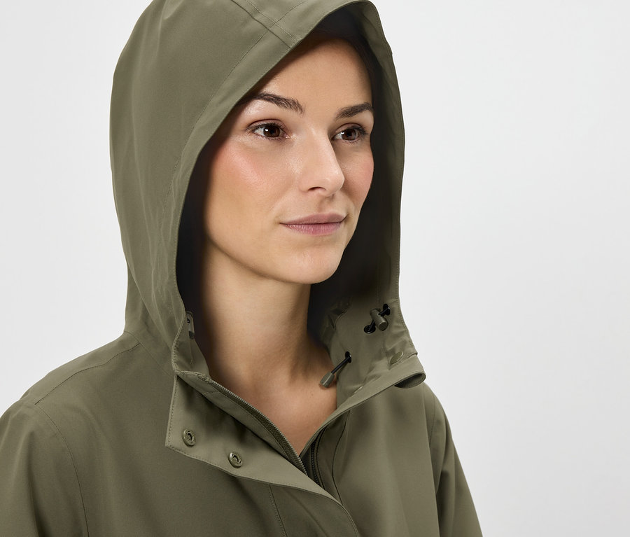 Femme aux cheveux bruns portant une veste à capuche vert olive.