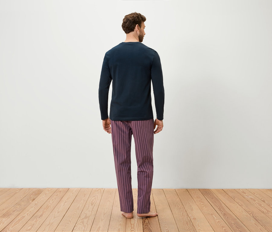 Un homme, vu de dos, porte un t-shirt à manches longues bleu marine et un pantalon de pyjama rayé violet.