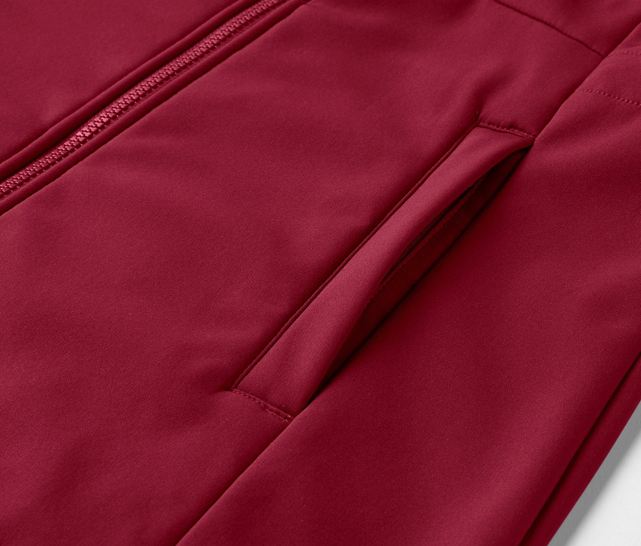 Gros plan sur un manteau en softshell rouge foncé avec fermeture éclair et poche.