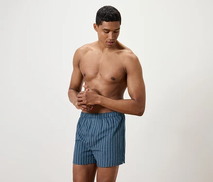 Un homme torse nu se frotte les mains, portant un caleçon boxeur bleu rayé.