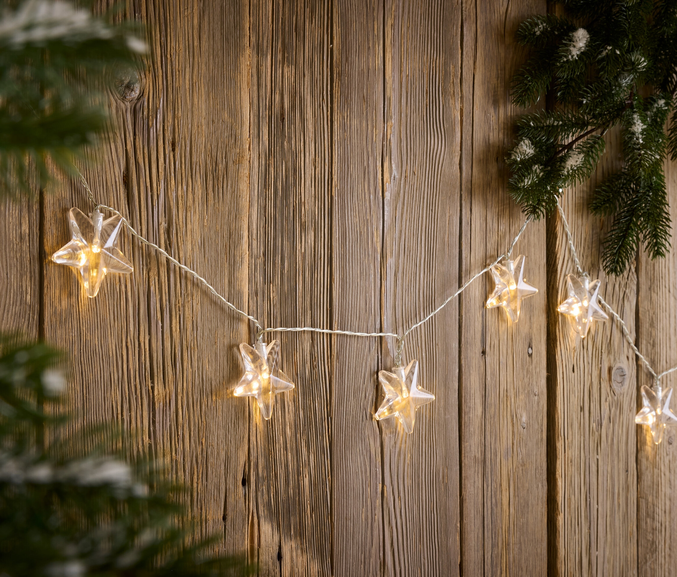 Une guirlande lumineuse en forme d'étoile est suspendue à un mur en bois à côté d'une branche de pin.