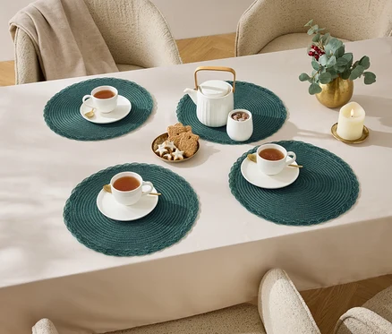 Quatre tasses de thé sur une table avec une nappe, une théière, un sucrier, des biscuits et une bougie.