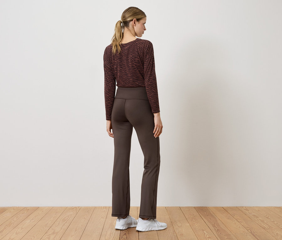 Femme portant un pantalon marron et un haut à manches longues, dos à la caméra.