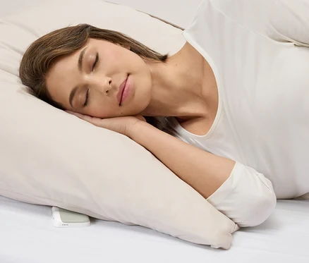 Une femme dort sur un oreiller à côté d'un appareil sonore blanc.