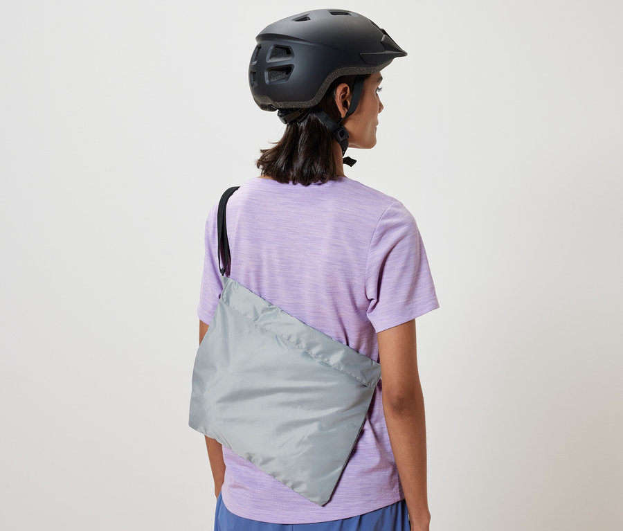 Une femme portant un casque de vélo a un sac à provisions pour vélo sur l'épaule.