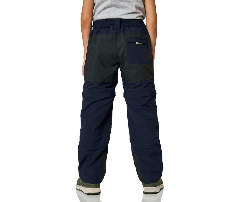 Enfant de dos portant un pantalon zip-off JAKO-O bicolore marine et gris foncé avec des chaussures vert olive.