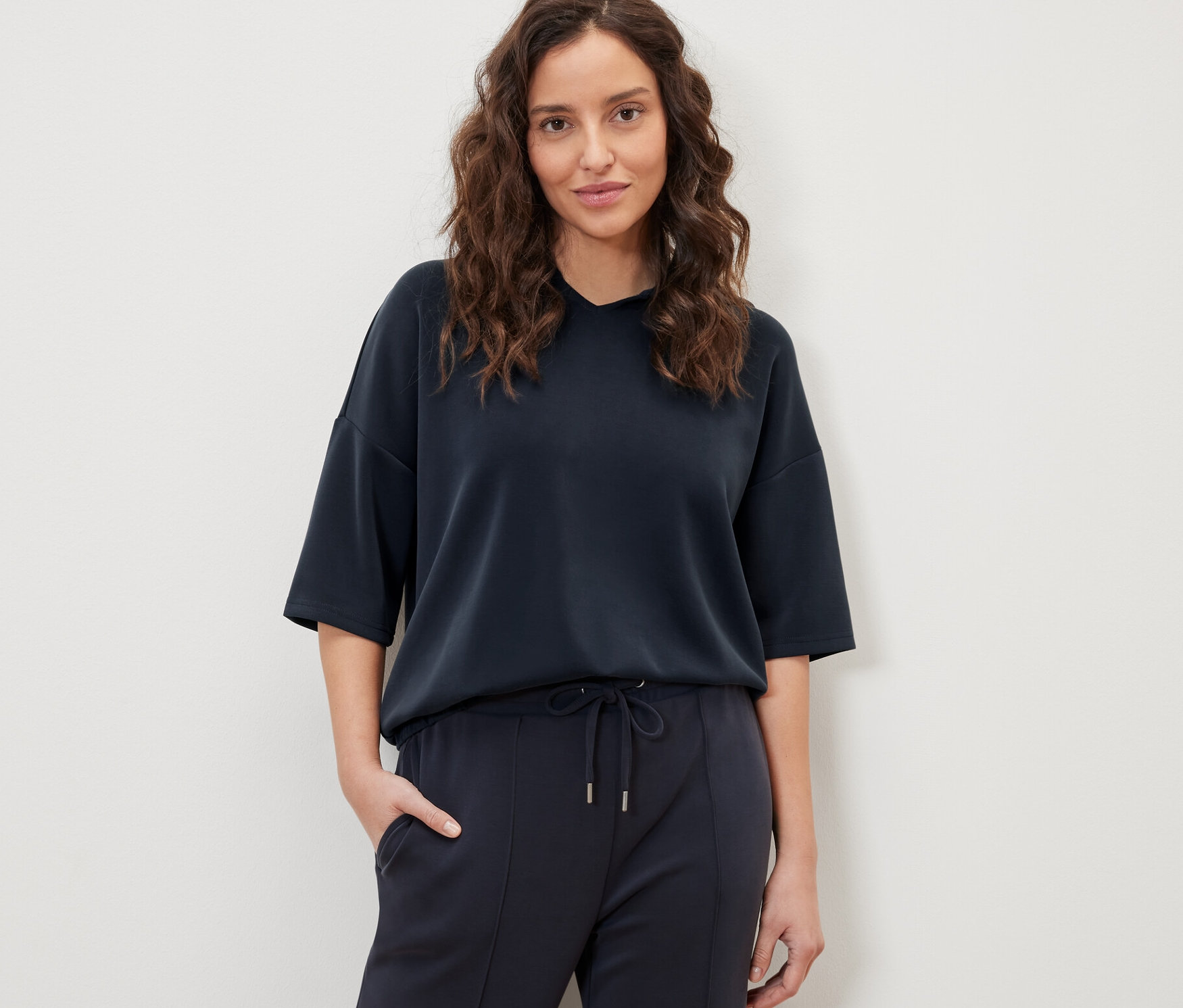 Femme posant en pull à capuche bleu foncé en mélange de modal et pantalon.