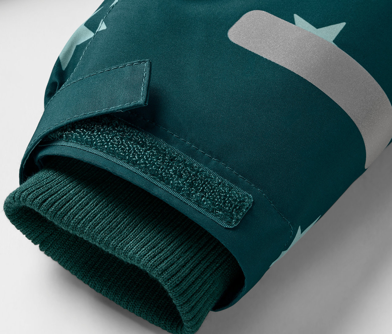 Détail d'une veste vert foncé avec poignet tricoté et élément réfléchissant.