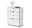 Commode métallique blanche « CN3 » avec 3 tiroirs et un abattant. Un vase avec une plante et un livre sont posés sur la commode.