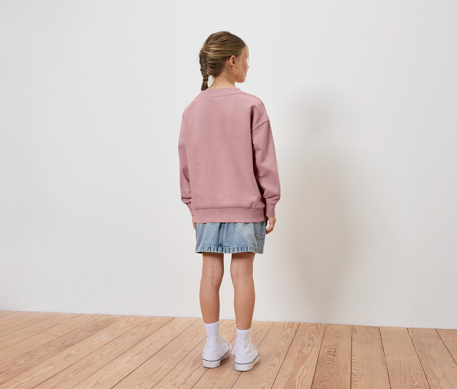 Une jeune fille, vue de dos, porte un sweat-shirt rose et une jupe en jean.