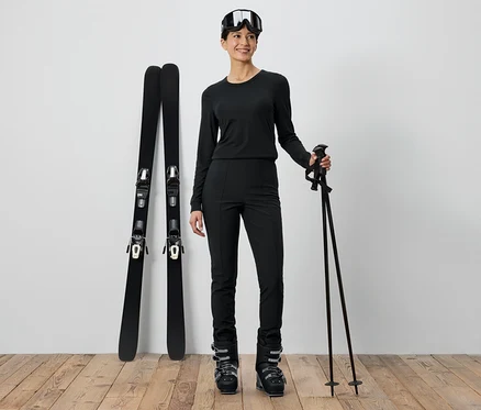 Femme en tenue de ski noire debout à côté de skis et de bâtons.