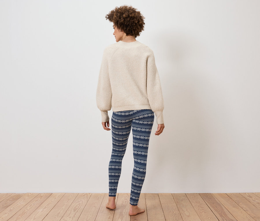 Vue de dos d'une femme avec une coiffure afro portant un pull crème et un legging bleu à motifs de flocons de neige.