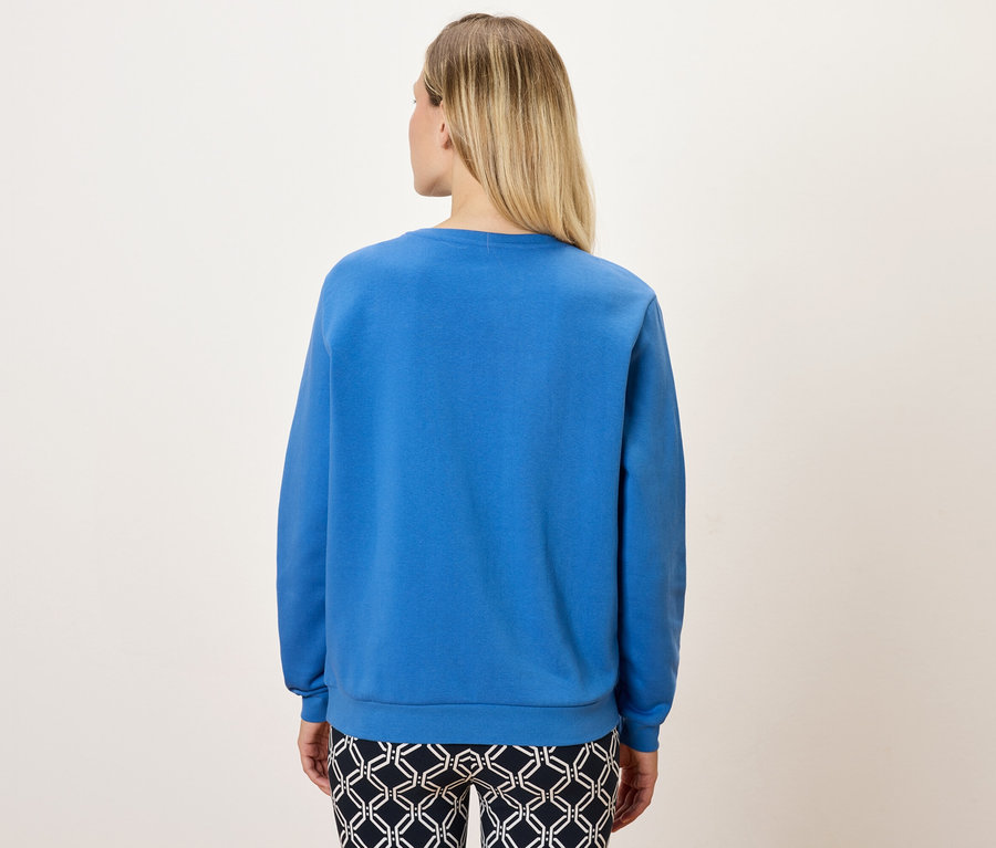 Vue arrière d'une femme blonde portant un sweat-shirt bleu et un pantalon à motifs.