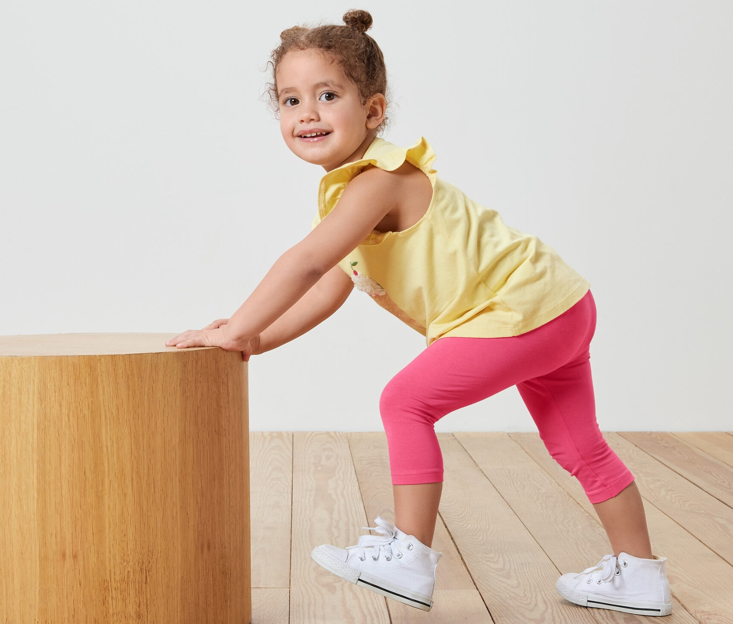 Une fille pousse une table cylindrique en bois, elle porte un legging 3/4 rose.