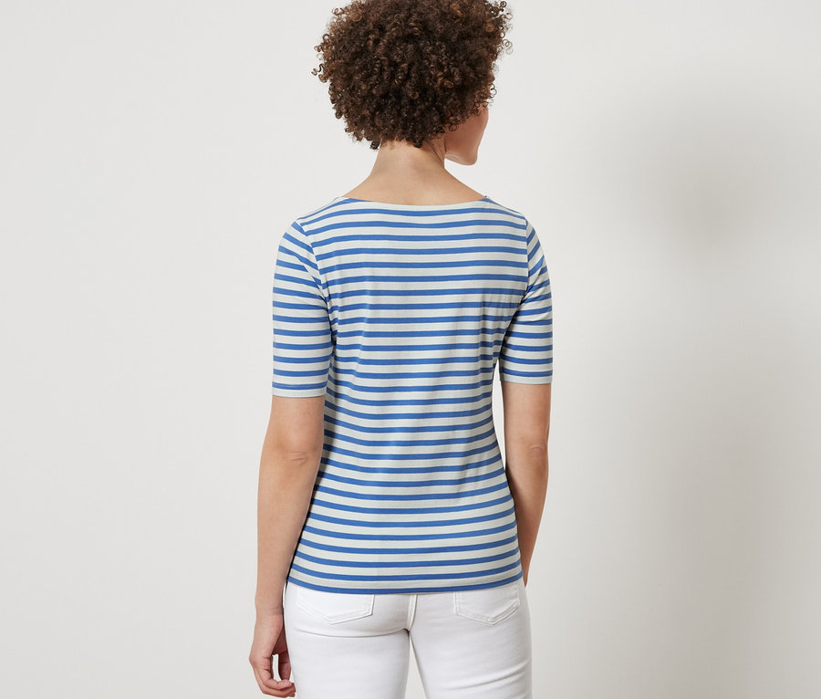 Vue arrière d'une femme aux cheveux bruns bouclés portant un t-shirt à rayures bleues et un jean blanc.