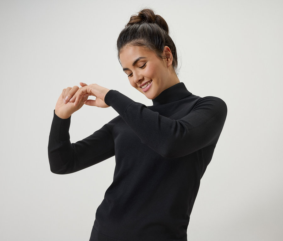 Femme souriant et posant dans un pull à col roulé noir.