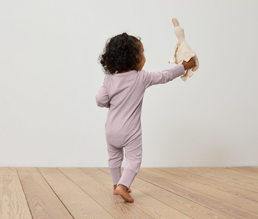 Un enfant en combinaison rose tenant une peluche de canard.