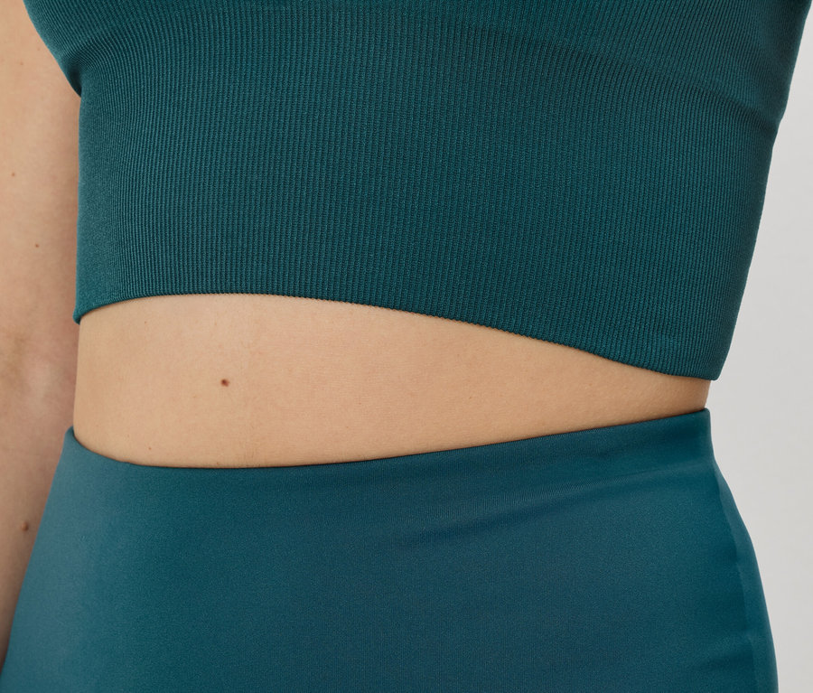 Gros plan d'une femme portant un haut de sport côtelé pétrole et un legging.